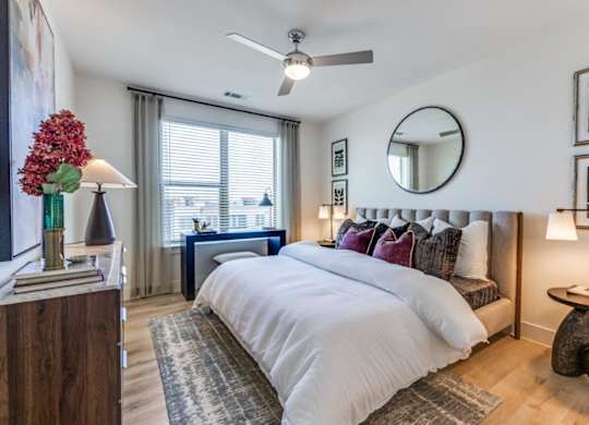 A bedroom with a large bed, a ceiling fan, and a mirror on the wall.