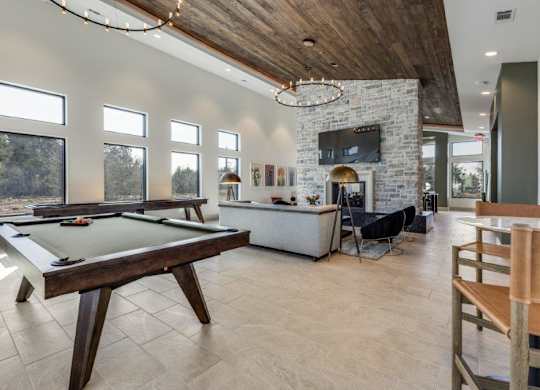 A pool table is in the middle of a room with a stone fireplace and a TV above it.