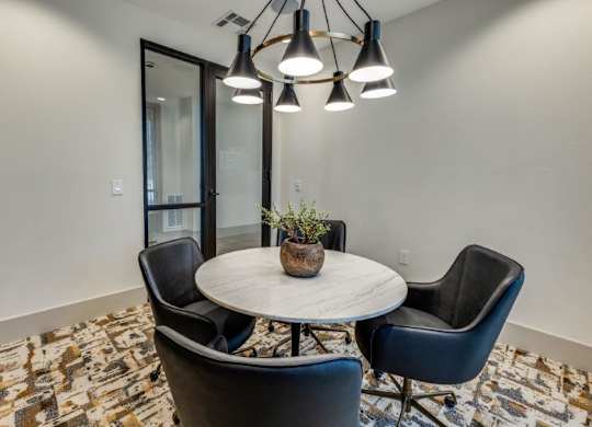 A round table with a potted plant on it and two chairs in a room with patterned carpeting.