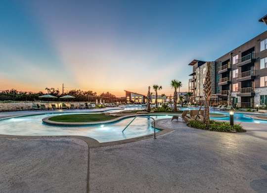 A large outdoor swimming pool surrounded by a concrete patio and a building in the background.