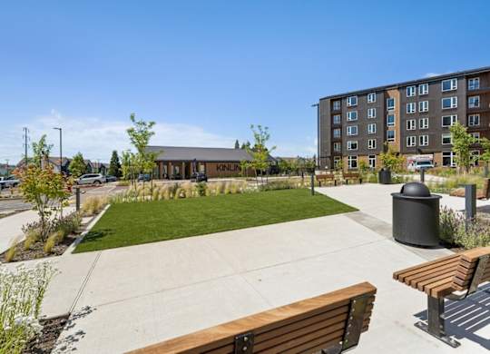 A sunny day at the KINLS apartment complex with a grassy area and benches.