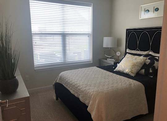 A bedroom with a bed, nightstand, and window with blinds.