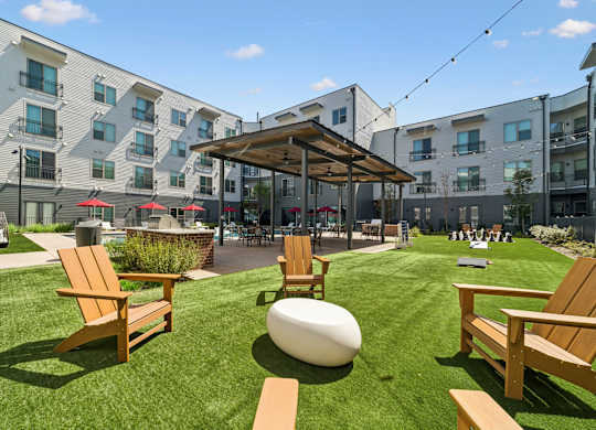 A sunny day at a modern apartment complex with a grassy area and wooden furniture.
