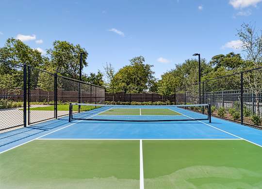 A tennis court with a blue and green surface surrounded by a black fence.