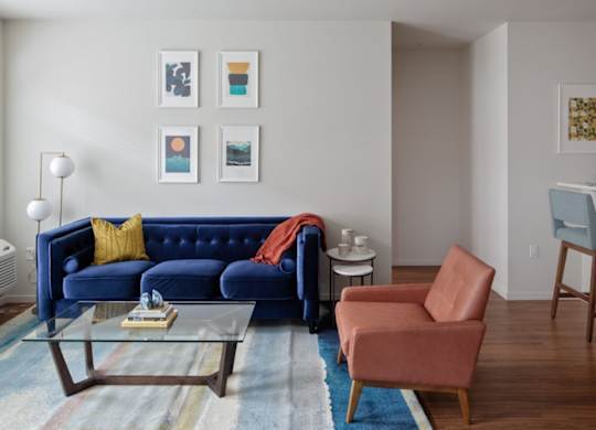 A living room with a blue couch, a red chair, and a glass coffee table.