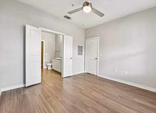 A room with a ceiling fan and light, wooden floors, and white walls with two doors open.