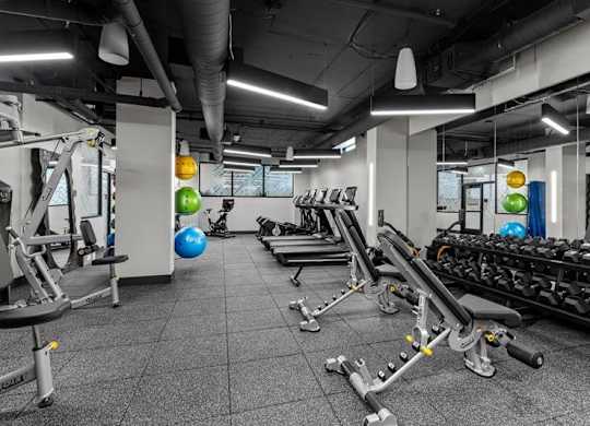 A gym with a variety of equipment including treadmills, weights, and exercise balls.