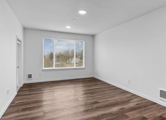 a living room with white walls and wood flooring and a window