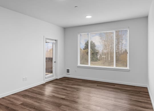 the living room of an apartment with a large window and wood flooring