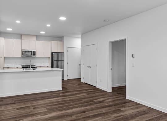 an empty living room and kitchen with white walls and wood flooring