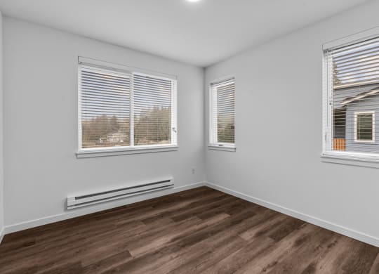 the living room of an apartment with wood flooring and three windows