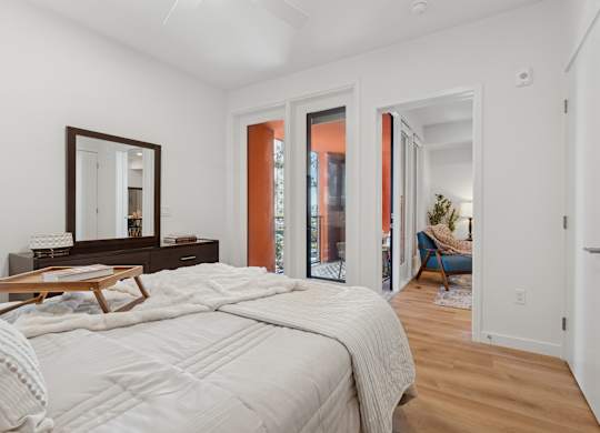 OnyxOnPark_SanDiego_CA_Model_1BR_ A bedroom with a large bed and a mirror on the dresser.