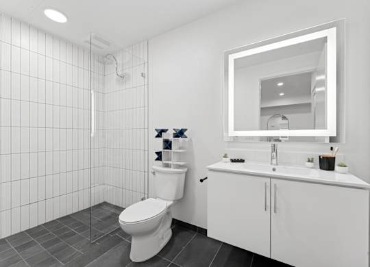 OnyxOnPark_SanDiego_CA_Model_1BR_ A white bathroom with a toilet, sink, and mirror.
