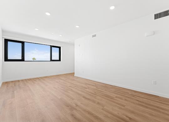 OnyxOnPark_SanDiego_CA_Vacant_2BR_ A room with wooden flooring and a window showing a blue sky with clouds.