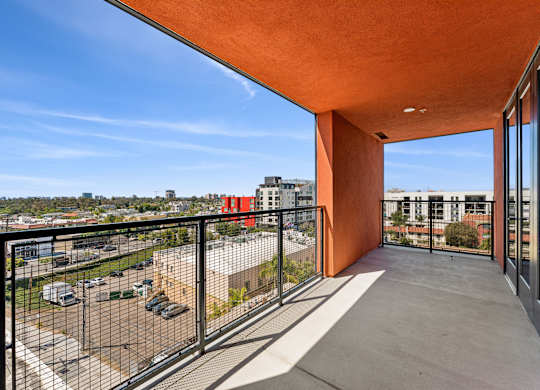 A balcony with a black railing and a view of a parking lot and buildings.