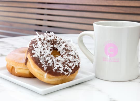 two donuts on a plate next to a coffee mug