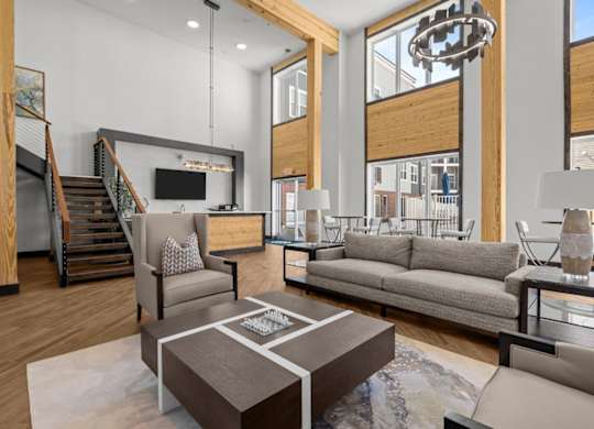 A modern living room with a staircase and a kitchen area in the background.