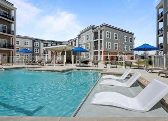 A pool area with white lounge chairs and a blue umbrella.
