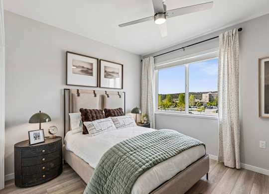 A bedroom with a large bed, a ceiling fan, and a view of the outdoors through a window.