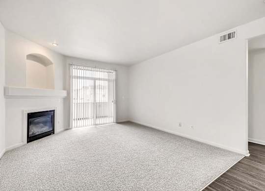 A large, empty room with a fireplace and a window with blinds.