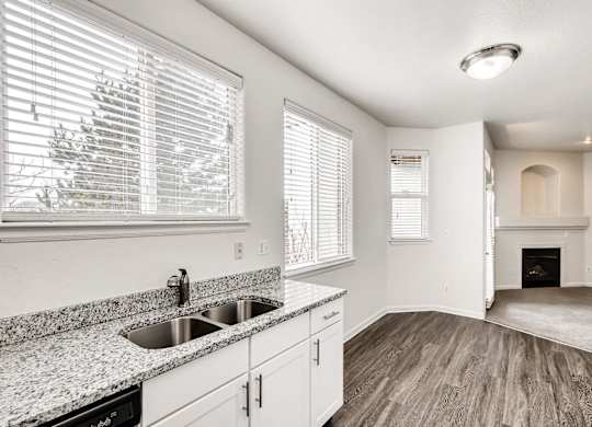 A kitchen with a sink, cabinets, and a window with blinds.