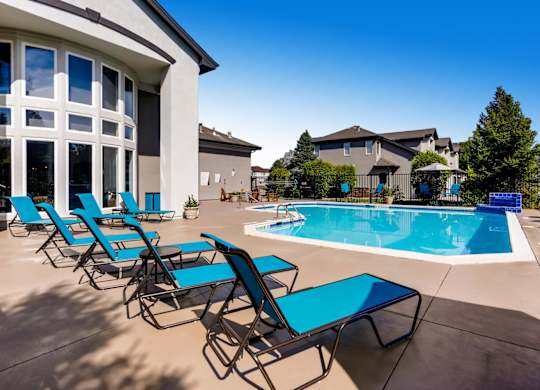 A poolside area with blue lounge chairs and a clear blue sky.