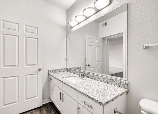 A bathroom with a granite countertop and white cabinetry.
