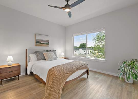 A bedroom with a bed, nightstand, and a potted plant.