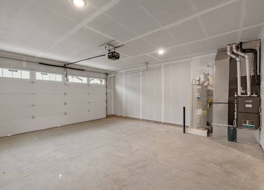 A large, empty room with a garage door on the left and a furnace on the right.