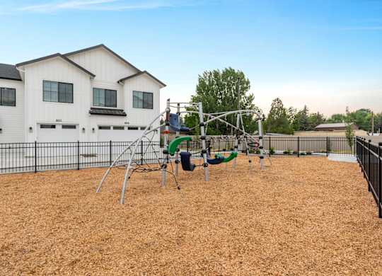 A playground with a swing set and a slide in front of a white house.