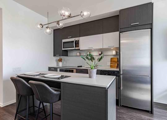 A modern kitchen with a stainless steel refrigerator, a black countertop, and a white backsplash.