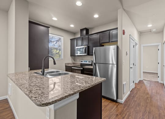 Little Tuscany Apartments & Townhomes - Kitchen with Dark Cabinets, Granite Countertops, Vinyl Wood Planking, White Door and Floor Trim, Stainless Steel Cabinets