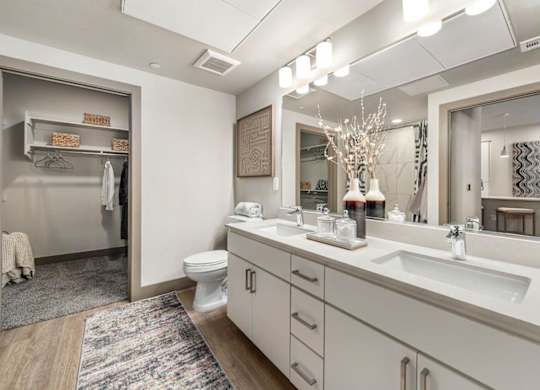 A bathroom with double white sink, toilet, and a mirror.