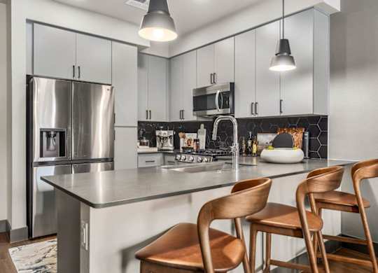 A modern kitchen with a stainless steel refrigerator, a stove, and wooden chairs.