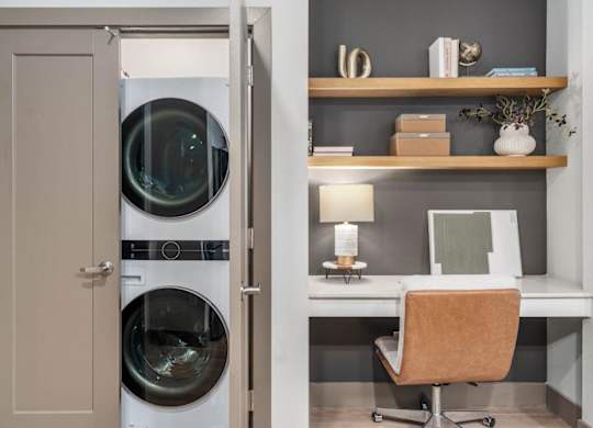 A laundry room with a washing machine and a small desk with a chair.