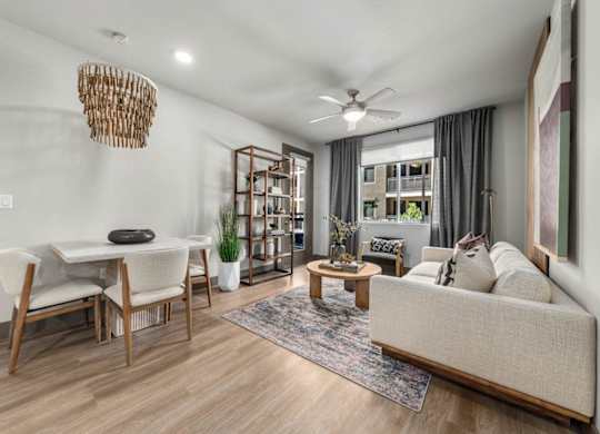 A living room with a white couch, a wooden dining table with chairs, a rug, and a ceiling fan.