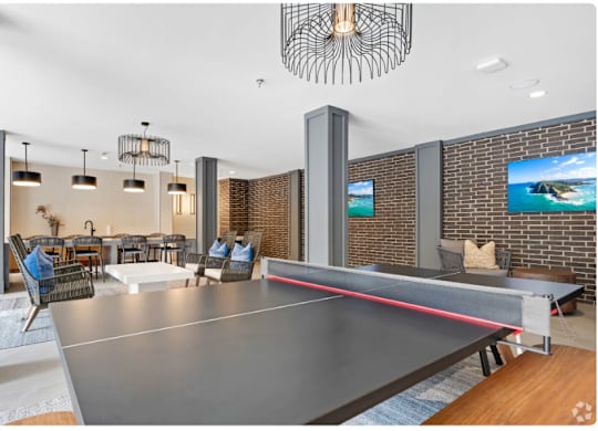A ping pong table is in the middle of a room with a brick wall and a television.