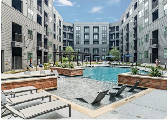 A pool surrounded by lounge chairs and planters in a courtyard.