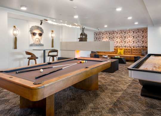 A pool table is in the middle of a room with a foosball table to the right.