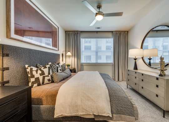A bedroom with a large bed, a dresser, and a ceiling fan.