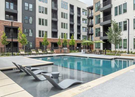 A swimming pool surrounded by modern buildings and lounge chairs.