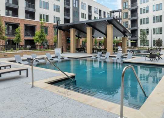 A pool surrounded by chairs and a building in the background.