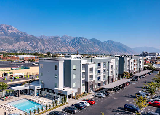 A parking lot with cars and a building with a pool in front of a mountain.