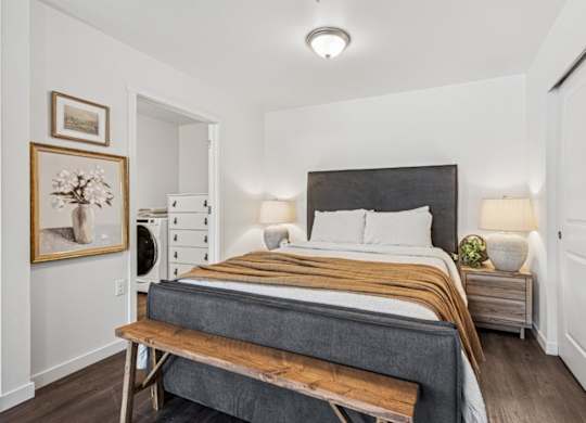 A bedroom with a bed, nightstand, and a painting on the wall.