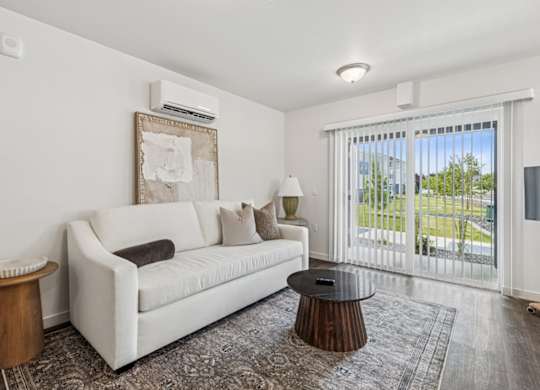 A white couch with a brown pillow is in the middle of a room with a window.