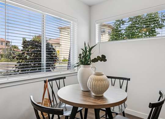 A table with a vase and a plant on it in front of a window.