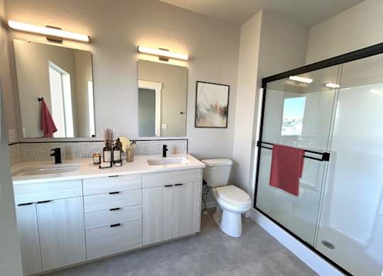 A bathroom with a white toilet, sink, and a red towel hanging on the glass door.