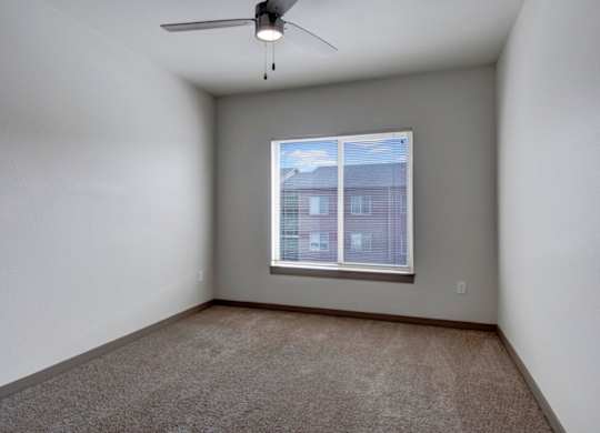 A room with a ceiling fan and a window showing a building outside.
