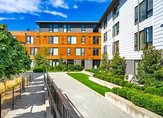 A modern building with a wooden facade is surrounded by a well-manicured lawn and a concrete pathway.