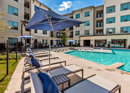 A pool area with sun loungers and umbrellas in front of a building.